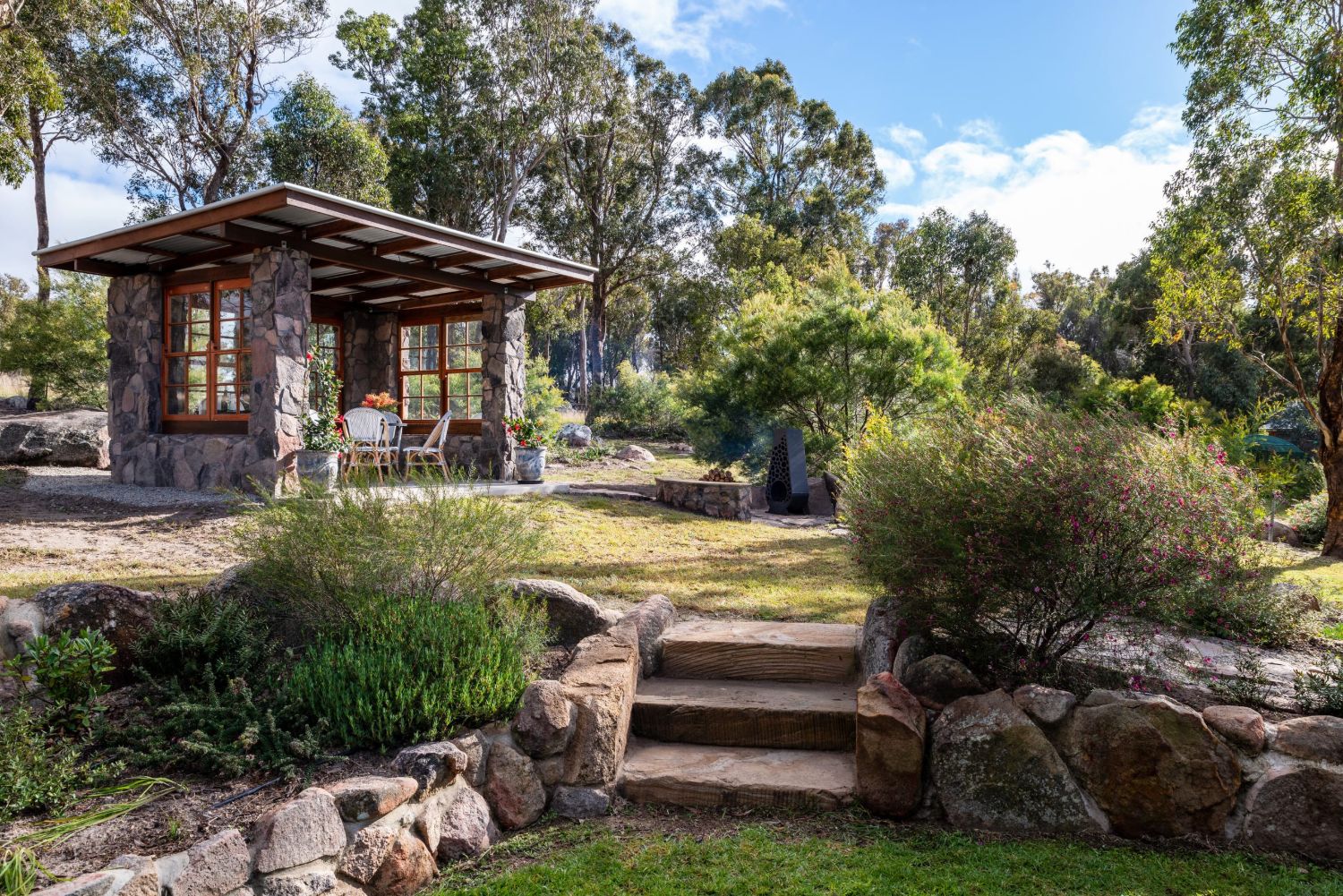 A stone bench in the native garden, the cottage beyond